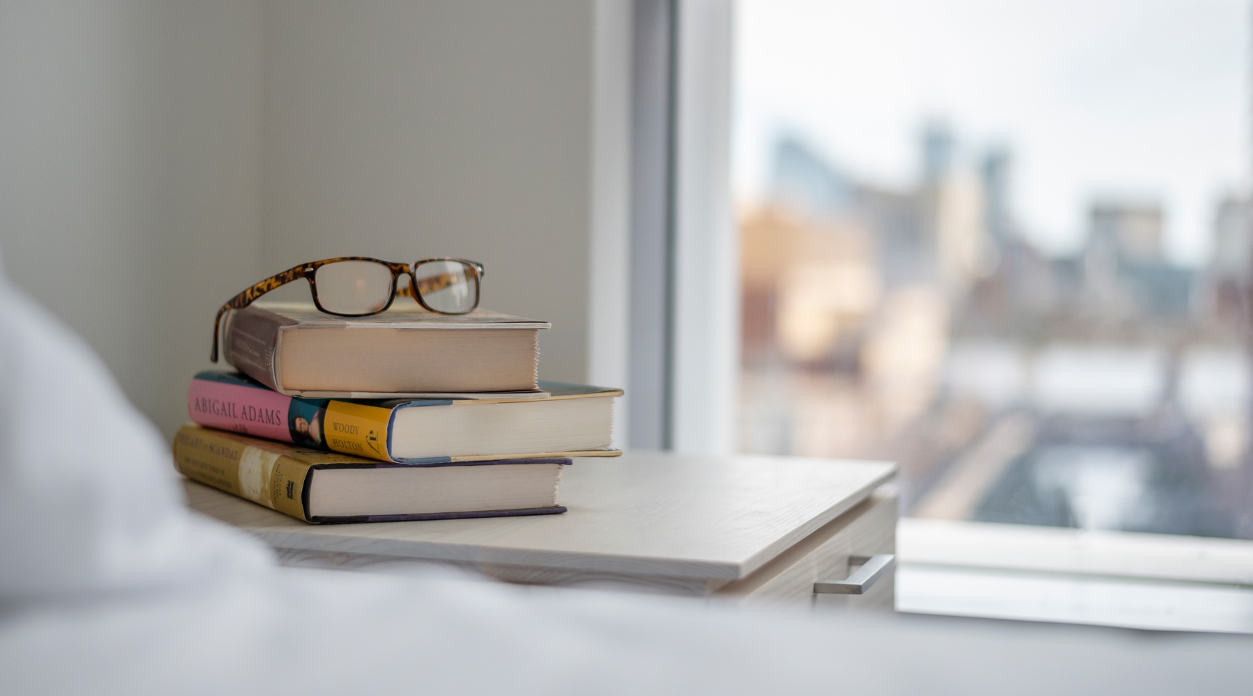 A stack of books and a pair of glasses resting on a neatly made bed, creating a cozy reading atmosphere